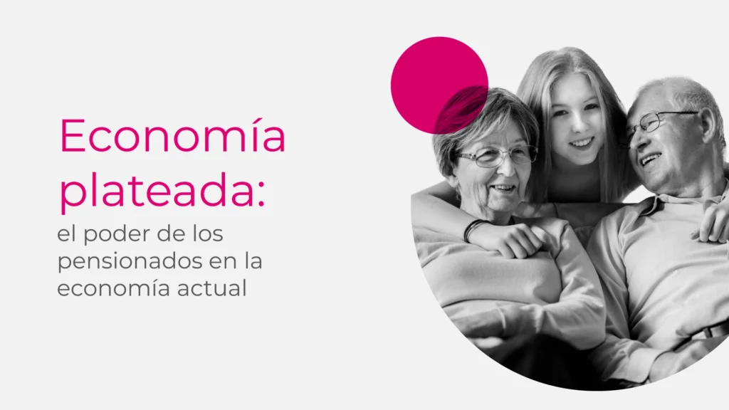 Fotografía en blanco y negro de una pareja de pensionados sentados, sonriendo y abrazados, con su nieta detrás abrazándolos por los hombros. La escena transmite unión familiar y felicidad. A la izquierda, sobre fondo claro, se lee el texto “Economía plateada: el poder de los pensionados en la economía actual” en tipografía moderna, acompañado de un círculo magenta como elemento gráfico decorativo.